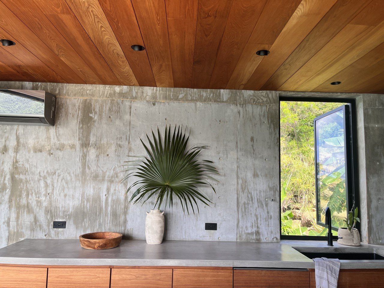 Kitchen with concrete counters, teak cabinetry and ceiling